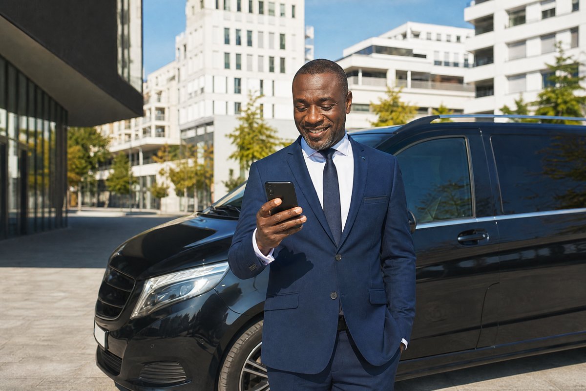 Chauffeur VTC français d'origine ouest-africaine souriant en regardant un avis 5 étoiles sur son téléphone à Lyon Confluence